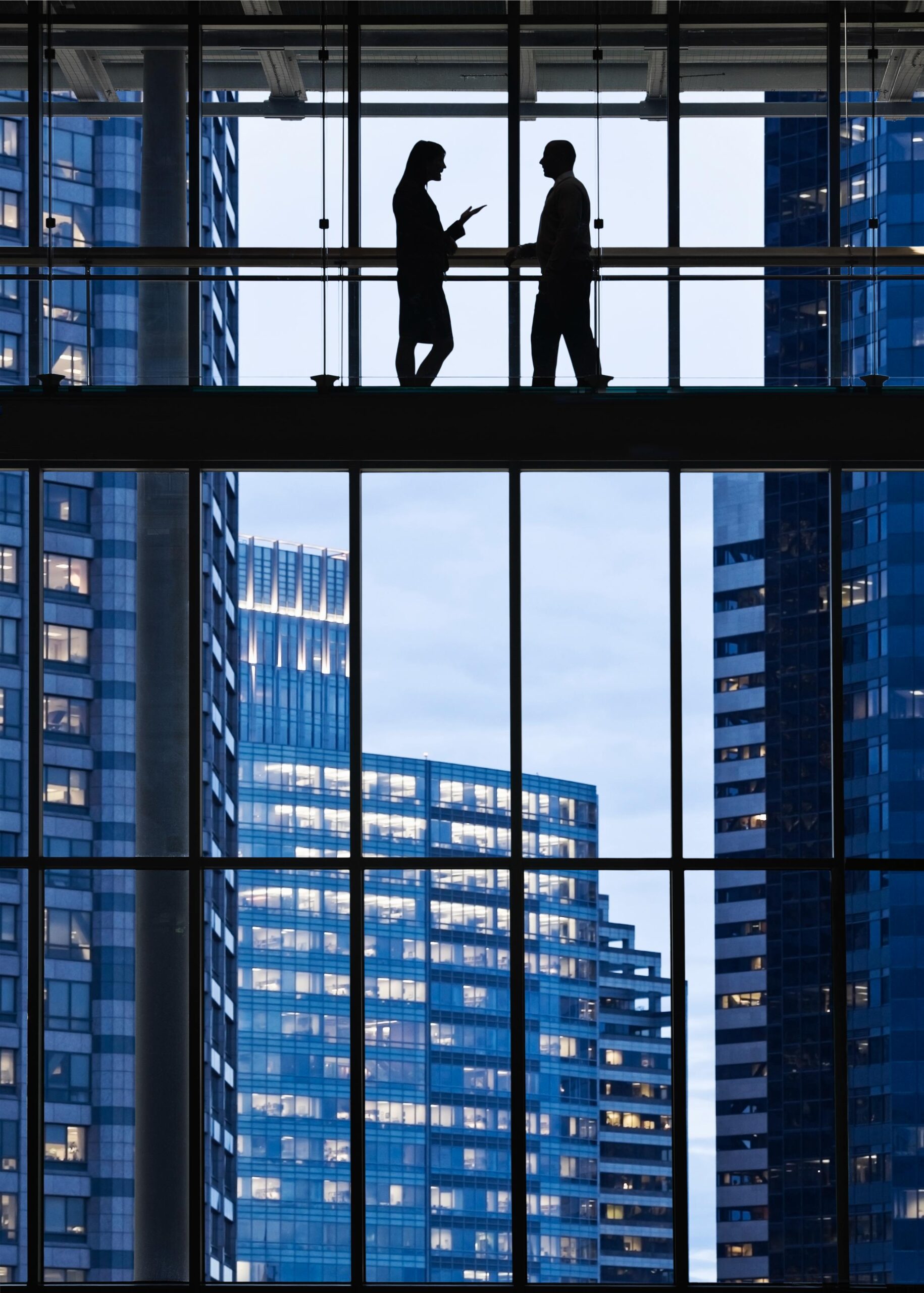 Two people talking on an elevated walkway, in silhouette against office towers